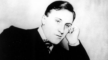 The picture shows Carl von Ossietzky in a black and white photograph. He is looking pensively into the distance with his head resting on his left arm.