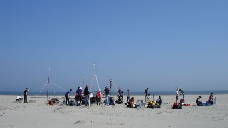 Many people perform measurements on a sandy beach.