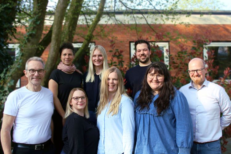 Auf dem Bild sind 8 Personen zu sehen, die frontal in die Kamera schauen.