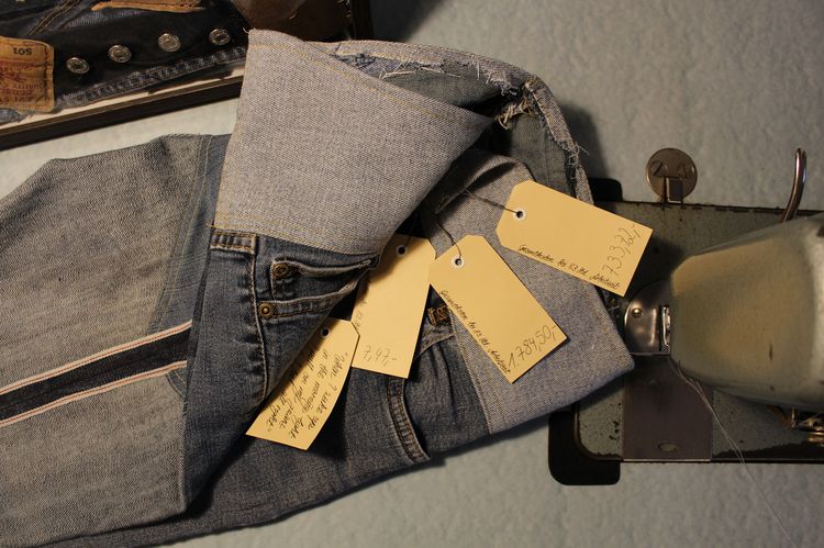 Das Bild zeigt eine Jeans, die mit verschiedenen Preisschildern ausgestattet ist. Eine Beschriftung lautet: "Gesamtkosen bei 83 Stunden Arbeitszeit: 1784 Euro und 50 Cent. 