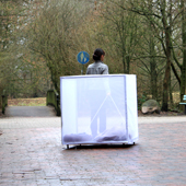 Foto des Projektes. Ein mit weißen Tüchern bespannter Kasten steht draußen. Dahinter eine Frau.