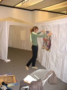 Foto des Projektaufbaus: Ein Mensch hängt die ausgebreiteten Plakate an einer Pavillionwand auf.
