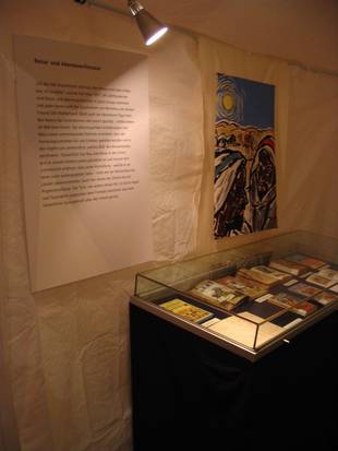 Foto der Ausstellung: Bücher liegen in einem Glaskasten, Plakate mit Informationen hängen an der Wand.