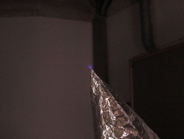 Foto einer geladenen Aluminiumspitze an der eine Funkenentladung in die Luft sichtbar ist.