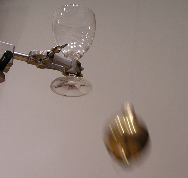 Foto einer Pendelmasse, die sich auf ein Glas zubewegt.