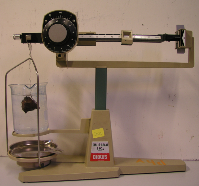 Foto einer Balkenwaage mit der die Gewichtskraft einer Masse in einer Flüssigkeit bestimmt wird.