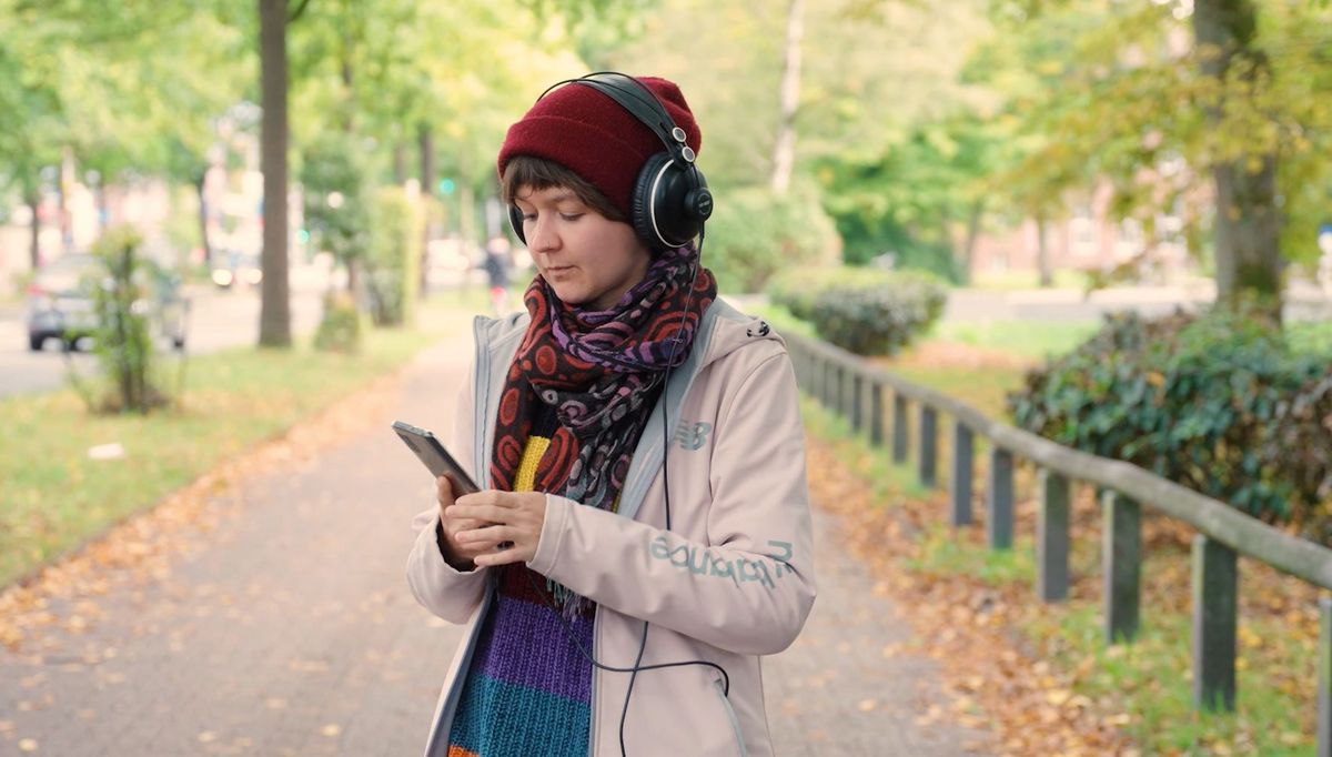 Eine Frau mit Kopfhörern und Smartphone draußen im Park