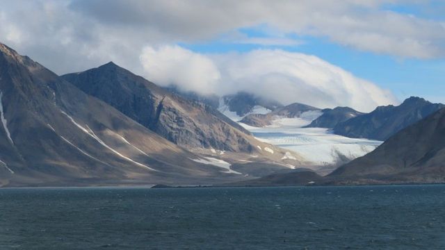 Photo of Hornsund on Spitsbergen, Norwary, with the glacier Gasbreen, in the background and clouds over the mountains.