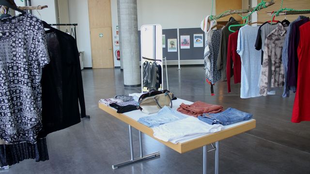 Das Foto zeigt die Kleidertauschbörse der NachDenkstatt 2022. Auf einem Tisch liegen Klamotten, auf Bügeln rechts und links im Bild weitere Kleidungsstücke.