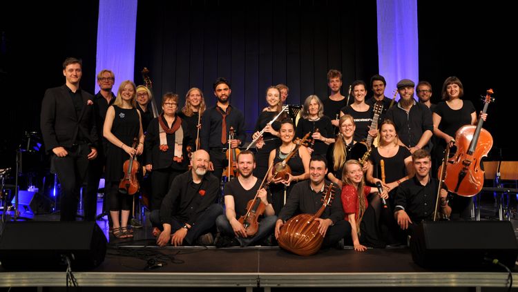 Das Bild zeigt Mitglieder des World Music Ensemble auf einer Bühne. Sie haben ihre Instrumente bei sich.
