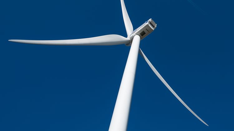 The rotors of a wind turbine, seen from below against the steel-blue sky. 