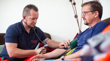 A community paramedic measures the blood pressure of a man in his home environment.
