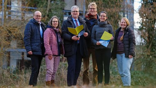 Die Gruppe im Grünen vor einem Uni-Gebäude, zwei Personen halten das Klimaschutzkonzept in den Händen. 