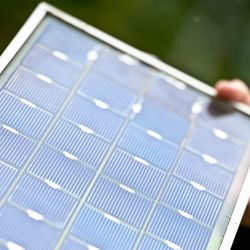 Schräger Blick auf ein Fotovoltaikmodul, Größe vielleicht 30 mal 60 Zentimeter,, das von einer Person in der Hand gehalten wird.
