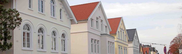 Eine Reihe von "Hundehütten"-Häusern in Oldenburg mit roten Ziegeldächern und gepflegten Gärten.