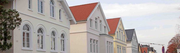  A row of "Hundehütte"-style houses in Oldenburg with red tile roofs and well-maintained gardens.