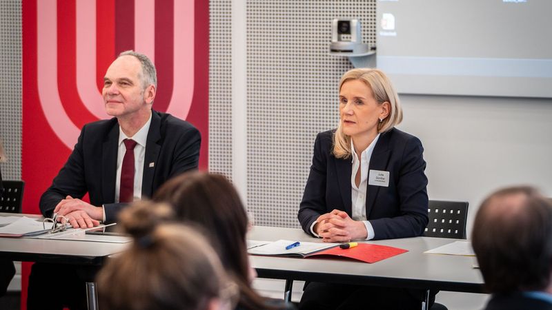 Das Bild zeigt Ralph Bruder und Jutta Günther. Sie sitzen als Tagungspräsidium den teilnehmenden Senatsmitgliedern gegenüber und leiten die Sitzung. Hinter ihnen wird eine Präsentation an der Wand gezeigt.