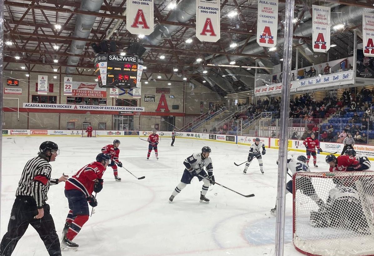 Eishockeyspiel in einer vollen Halle, Spieler kämpfen um den Puck vor dem Tor.