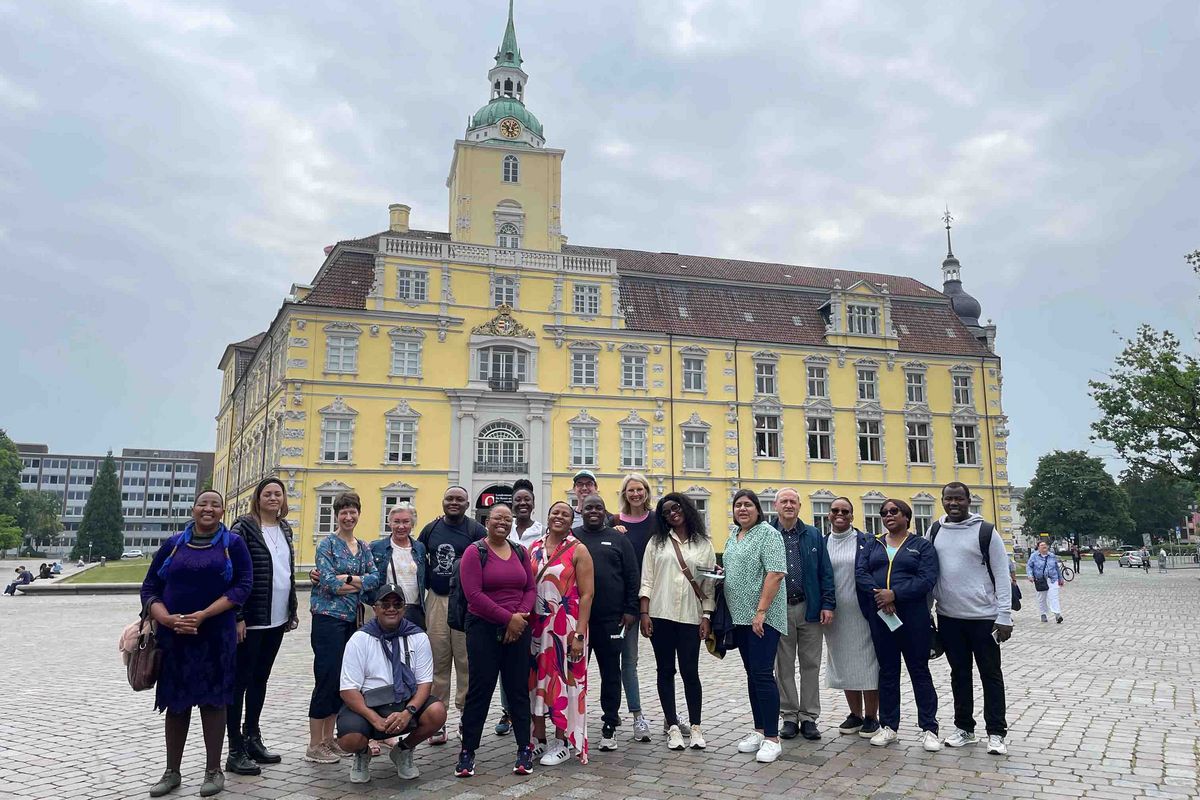 A group of people posing in front of the Oldenburg Castle. In the background the yellow castle with its distinctive tower.