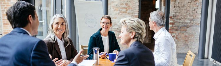 Mitarbeitende sitzen um einem Tisch herum und diskutieren. 