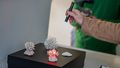Four small coral skeletons stand on a small table. An arm can be seen from the side holding a kind of torch. This illuminates a coral in red. 