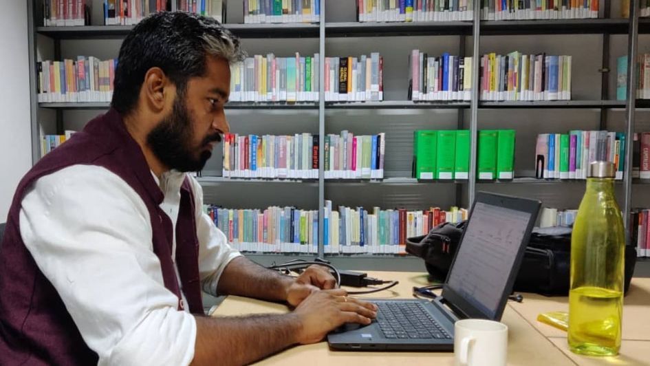 Ein Mann sitzt in der Bibliothek des Tata Institute of Social Sciences und arbeitet an einem Laptop.