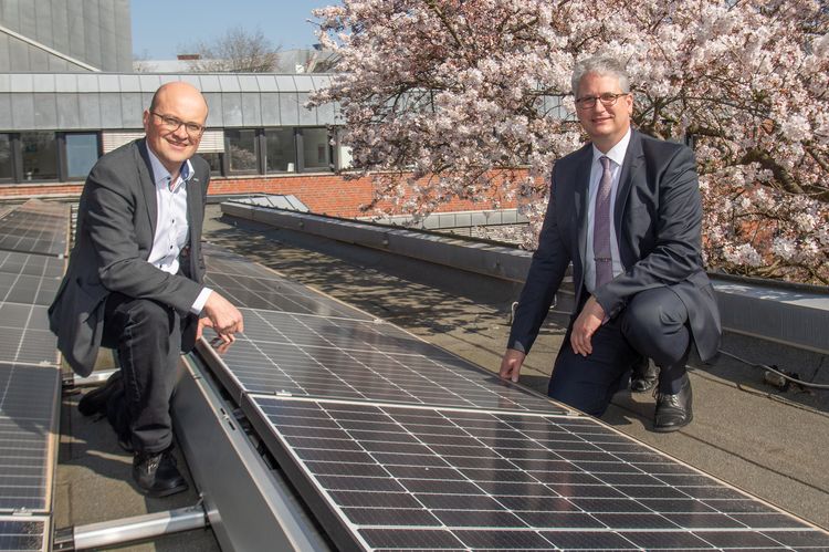 Herr Möllers und Herr Stahlmann knien auf dem Dach der Uni neben einem neu installierten PV-Modul.