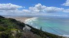 Eine Panoramansicht auf eine Küstenlandschaft mit grünen Hügeln, einem langen Sandstrand und dem türkisfarbenen Meer.