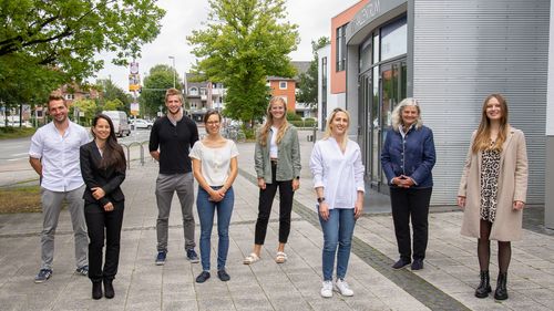 The eight people are standing in front of the lecture theatre centre.
