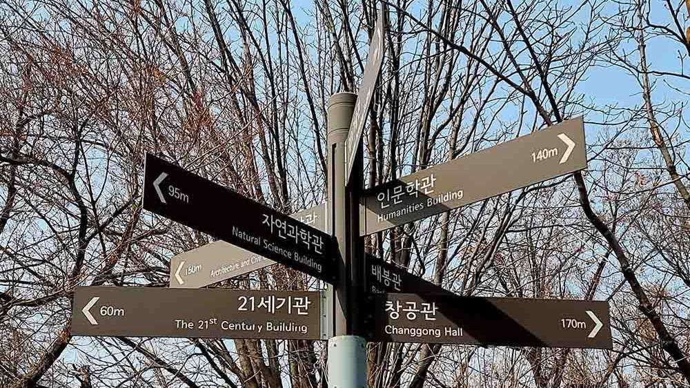 Ein Wegweiser auf dem Campus der University of Seoul mit Schildern in koreanischer und englischer Sprache.