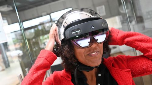 EA young woman presents the prototype of the smart helmet: she wears virtual reality goggles and a shiny silver bicycle helmet.