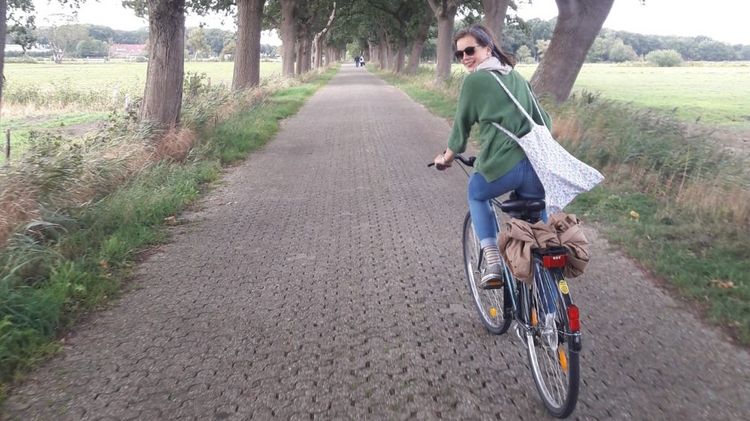Frau fährt mit dem Fahrrad entlang einer kleinen, von Bäumen gesäumten Straße und blickt sich nach hinten um.