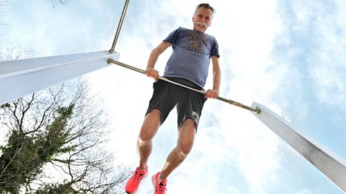 Martin Hillebrecht leans on a horizontal bar. Because the photo was taken from the ground, you can see the sky above him.