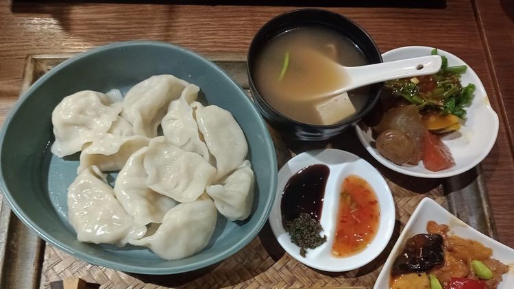 A tray with several plates and small bowls filled with dumplings, a soup, sauces and other side dishes.