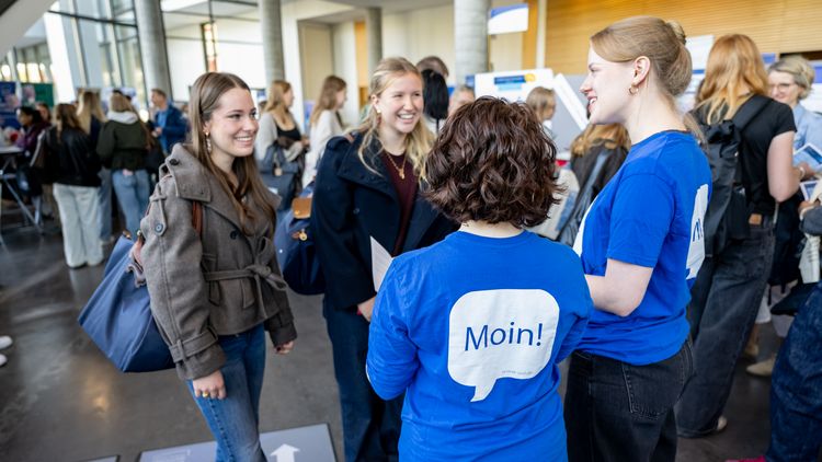 Two women wearing blue T-shirts with ‘Moin’ written on them are talking to two young women.