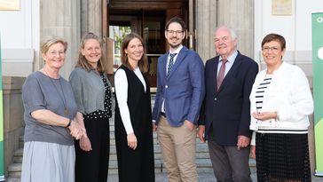 The picture shows the six people mentioned. They are standing in front of the entrance to the Alte Stadtkasse Oldenburg and smiling at the camera.