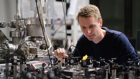 A young man sits in front of a complicated set-up of various physical devices.