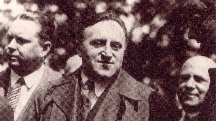 The picture shows Carl von Ossietzky next to other men. He is wearing a suit, tie and coat.