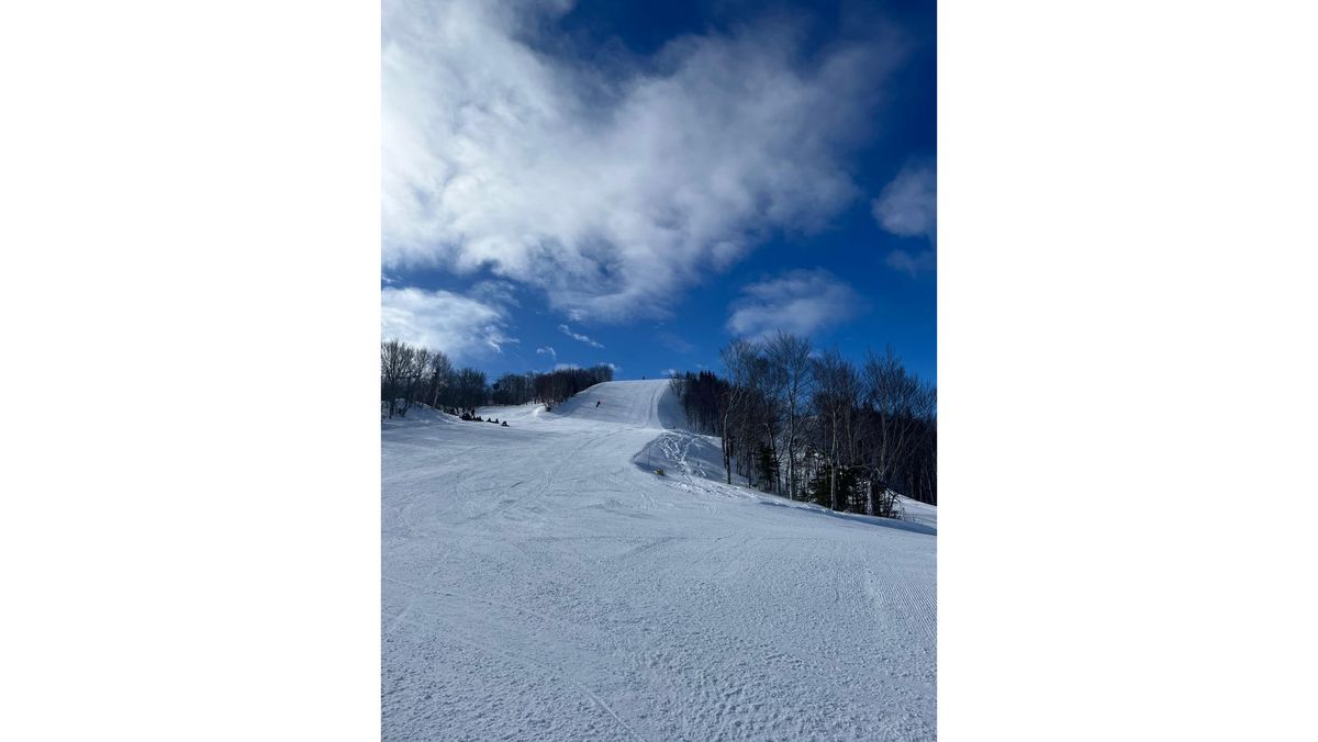 Verschneite Skipiste bei blauem Himmel, umgeben von winterlichen Bäumen.