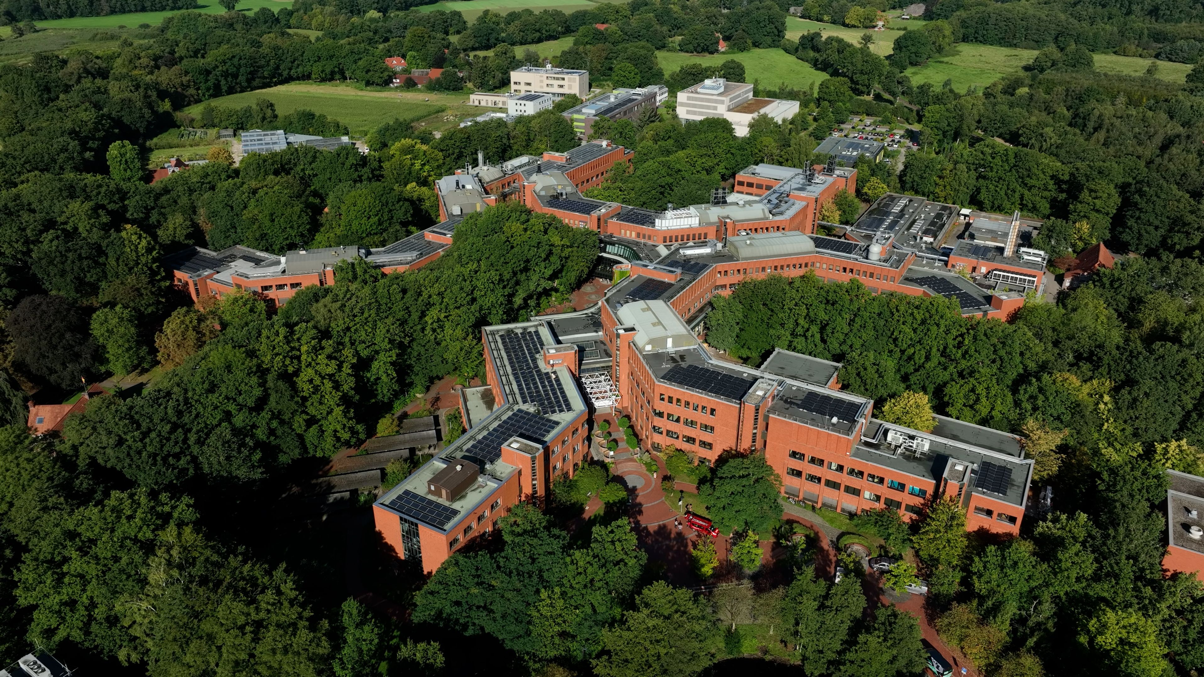 Aerial view of the main building, surrounded by many trees and green spaces, with other university buildings in the background.