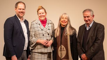 Four people in business attire stand next to each other and look into the camera.