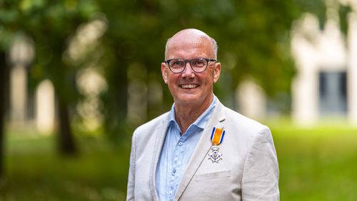 Ein Mann steht auf einer Wiese und trägt einen weißen Anzug mit einem Orden im Jackett.