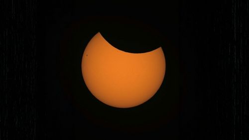 The reddish, glowing sun is obscured by the moon in its upper quarter.