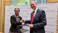 The Vice Chancellor of Nelson Mandela University (NMU), Prof. Dr. Sibongile Muthwa, and the President of the University of Oldenburg, Prof. Dr. Ralph Bruder, shake hands while looking into the camera. In their respective left hands they hold the new cooperation agreement. In the background is a display with the lettering and logo of the NMU.