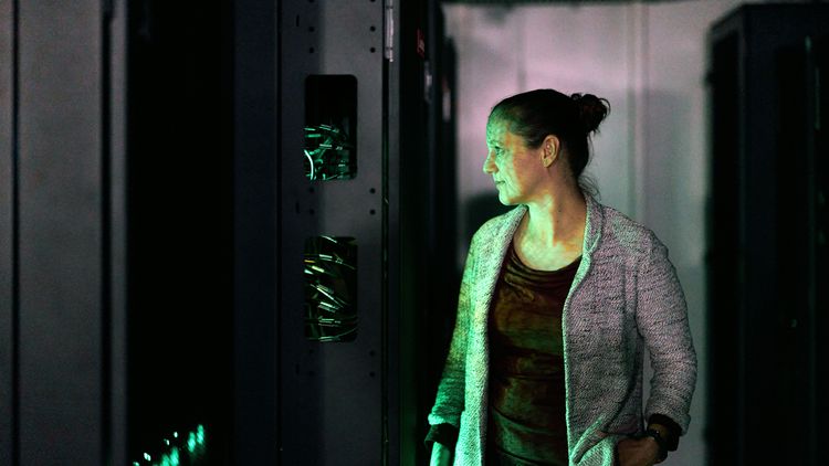 Sinikka Lennartz stands in the server room, her face illuminated in green. 