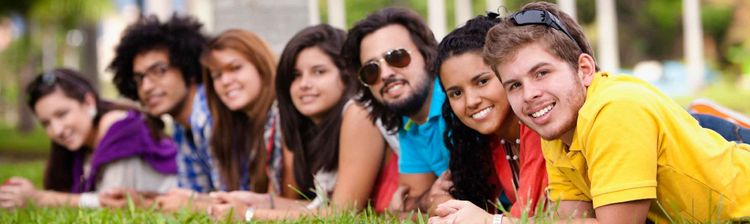 Eine Gruppe von sieben jungen Menschen liegt lächelnd auf einer grünen Rasenfläche.