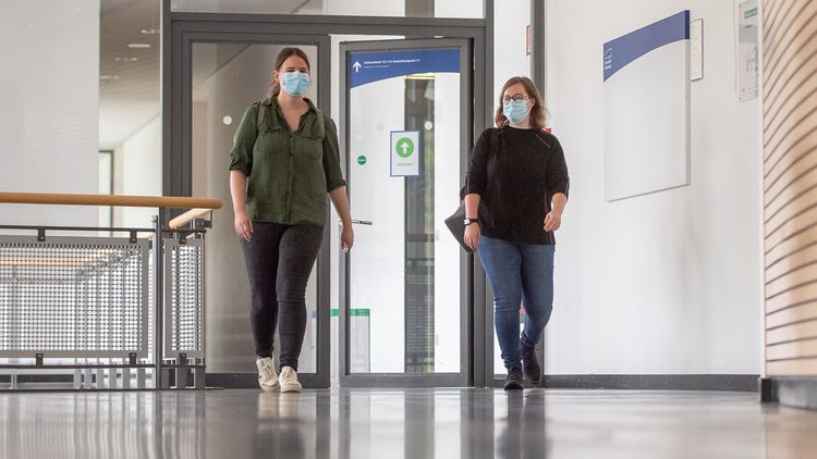 Two women wearing masks walk through the foyer of the lecture hall building A14.