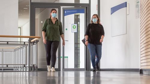 Zwei Frauen mit Masken gehen durch das Foyer des Hörsaalgebäudes A14.