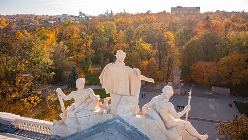 Aerial view looking over the roof of the university building with statues of three river goddesses onto an autumnal park, where the statue of Ivan Franko also stands. 