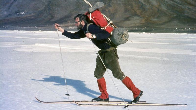 Historisches Foto aus dem Jahr 1969: Arktisforscher Ko de Korte ist auf Skiern in der Diskobucht, Spitzbergen, unterwegs. Er trägt einen roten Rucksack und rote rote Gamaschen. Im Hintergrund sind Berghänge zu erkennen.